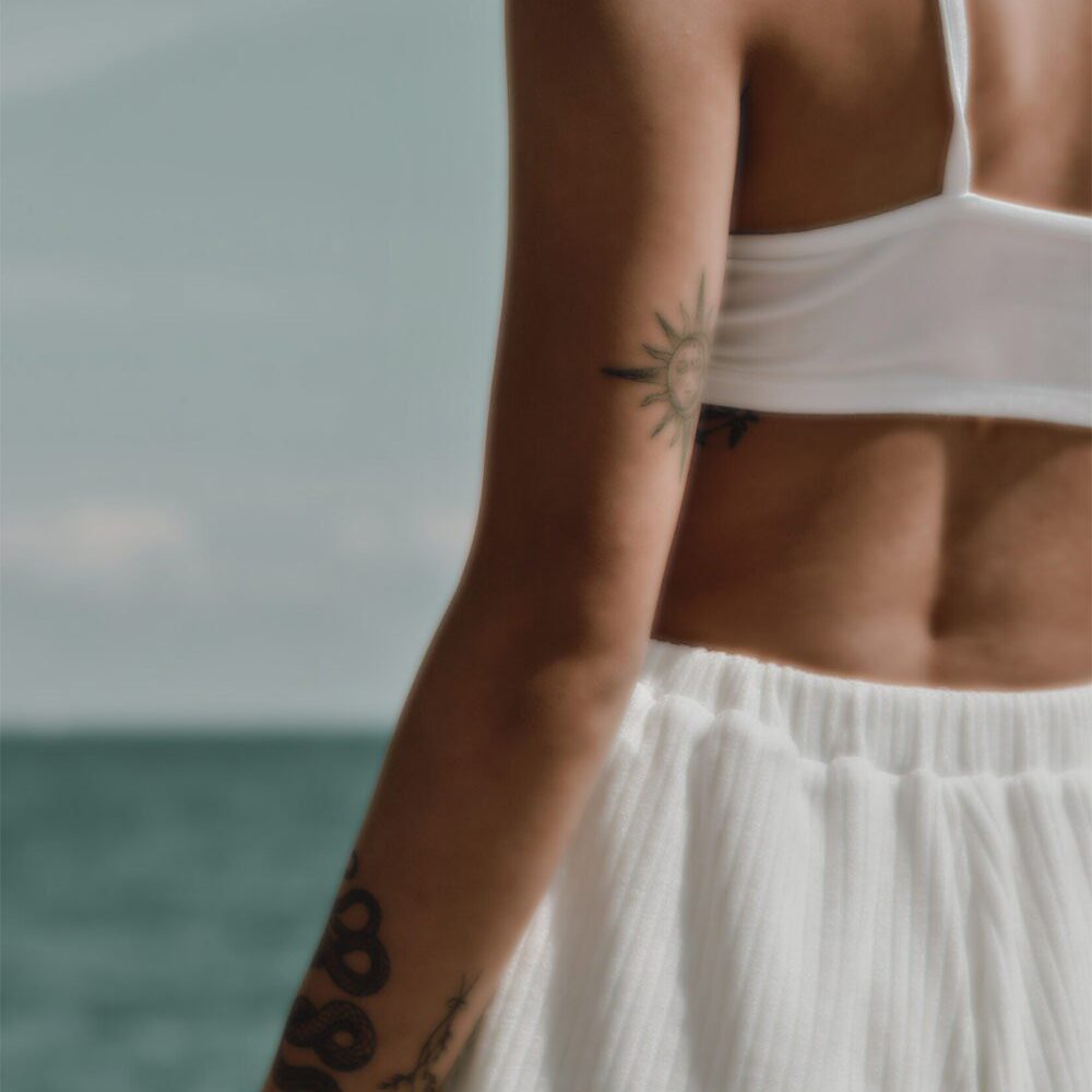 Back of a woman at the beach, she has a tattoo on the back of his arm
