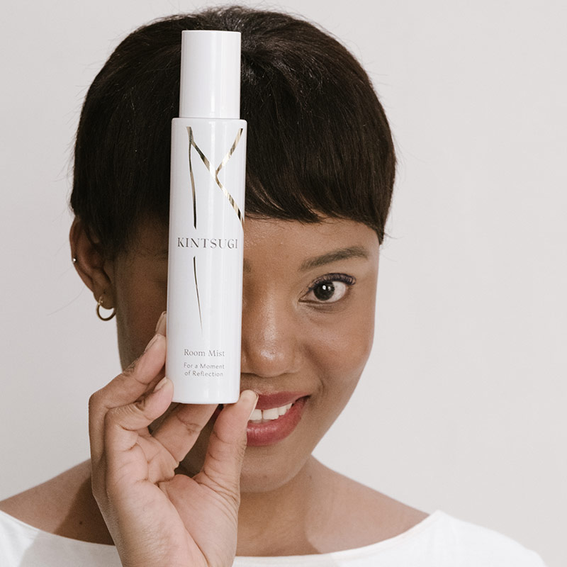 Woman holding room mist infront of her face, whilst smiling