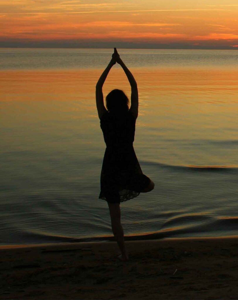 Woman meditating on the beach and you can see the sunrise in the background