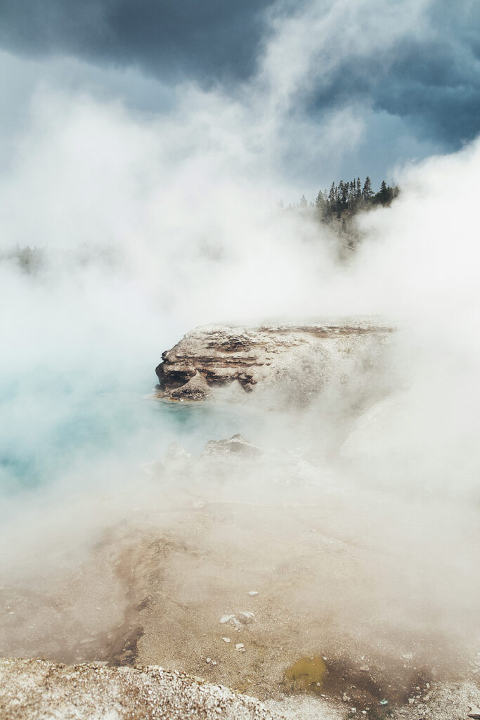 Mist drifts over rocks by a bright blue hot spring