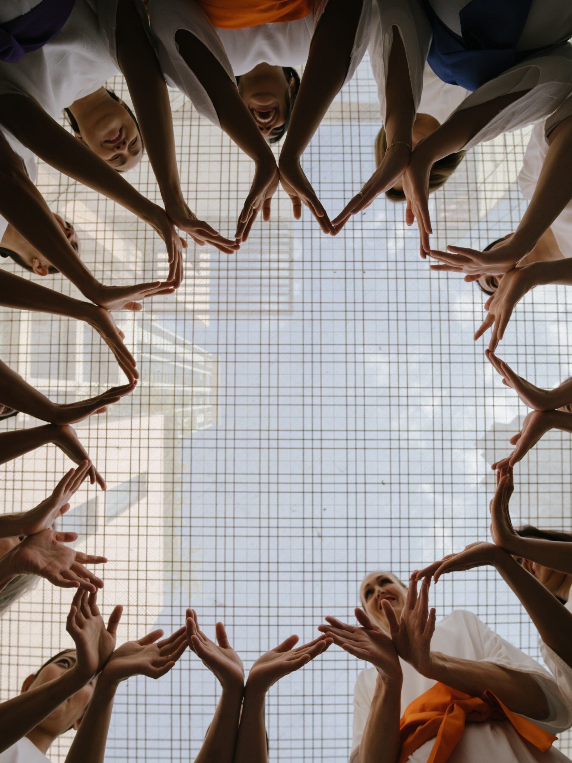 A community of people holding both hands together to make a big circle, taken from the floor so picture is facing the ceiling